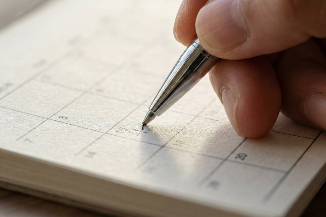 上質な紙のカレンダーにペンで予定を書き込む手元のアップ