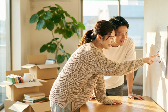 引っ越しの準備で段ボールを積みながらカレンダーを確認する日本人カップル