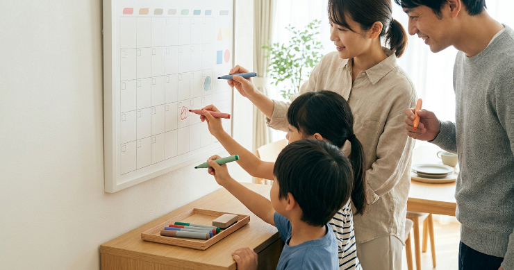 色分けした家族カレンダーに予定を書き込む日本人家族